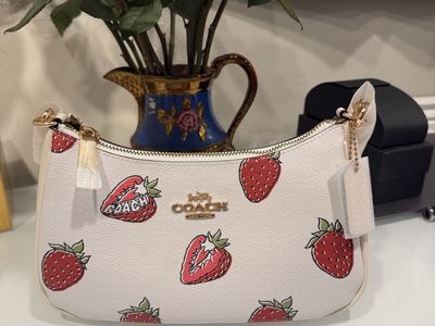 Coach leather tote with playful cherry motif. Red-accented handles and gold logo hardware. Structured silhouette suitable for da