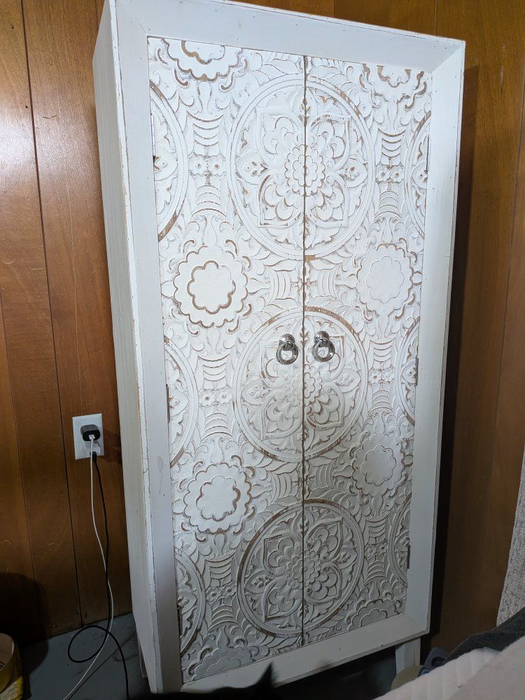White distressed wooden storage cabinet with decorative carved doors