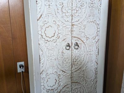 White distressed wooden storage cabinet with decorative carved doors