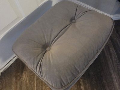 Tufted ottoman. Gray color. Has two buttons on top and piping around edge. Square shape.