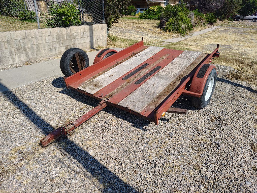 Red Utility Trailer - Flatbed, Single Axle with Wood Deck and Spare Tire.