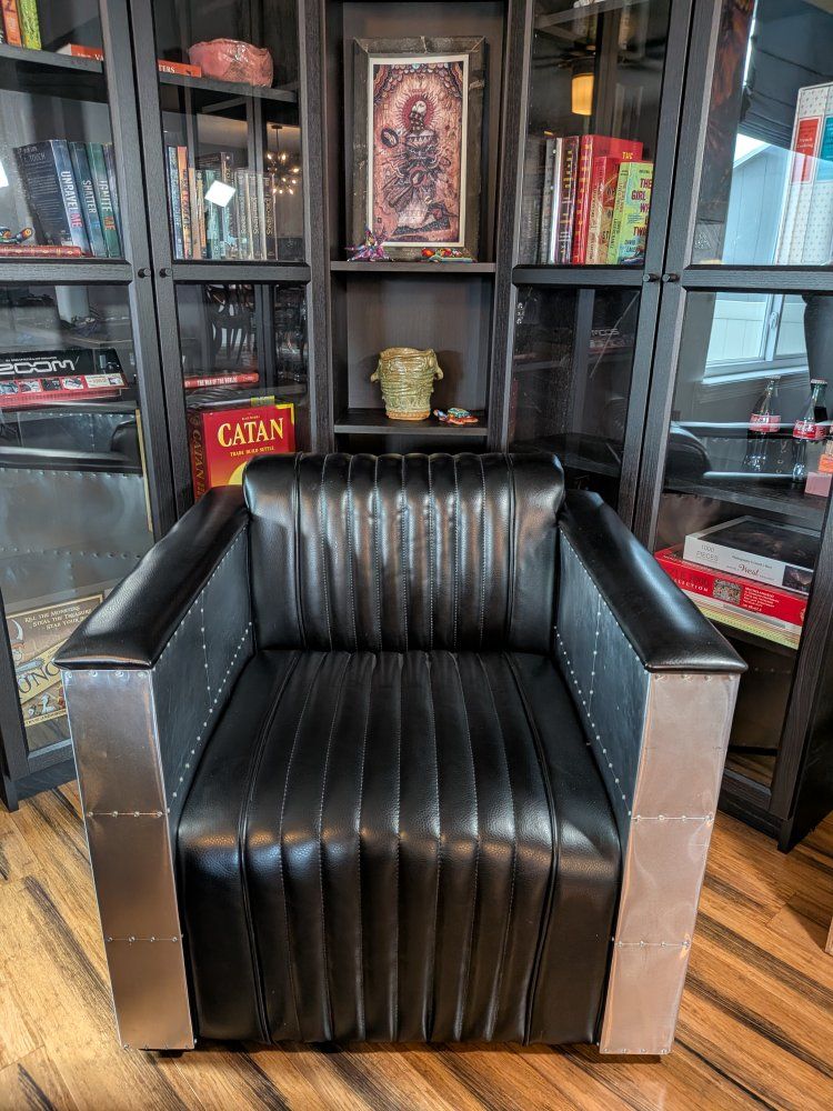 This industrial-style Strick & Bolton Vindicator armchair features channel-stitched black upholstery encased in aluminum panels