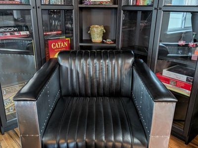 This industrial-style Strick & Bolton Vindicator armchair features channel-stitched black upholstery encased in aluminum panels