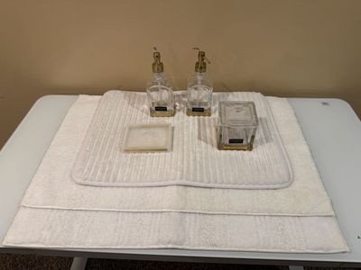 Tahari Home 4-Piece Clear Glass & Gold Bathroom Vanity Set - Soap Dispenser, Tray, Jar and 3 white bathroom rugs.