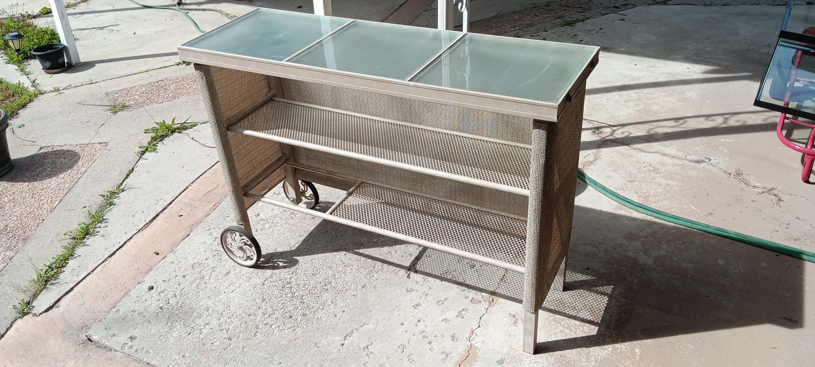 Glass top outdoor serving cart with shelf, on wheels, 55 3/4" x 18 3/4" x 39 1/2" tall.