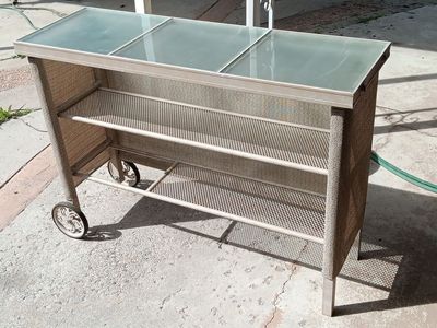 Glass top outdoor serving cart with shelf, on wheels, 55 3/4" x 18 3/4" x 39 1/2" tall.