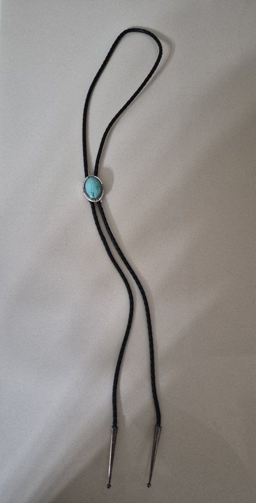 Native American style bolo tie features a turquoise stone set in a sterling silver bezel with braided leather cord.