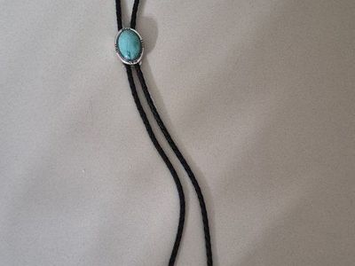 Native American style bolo tie features a turquoise stone set in a sterling silver bezel with braided leather cord.
