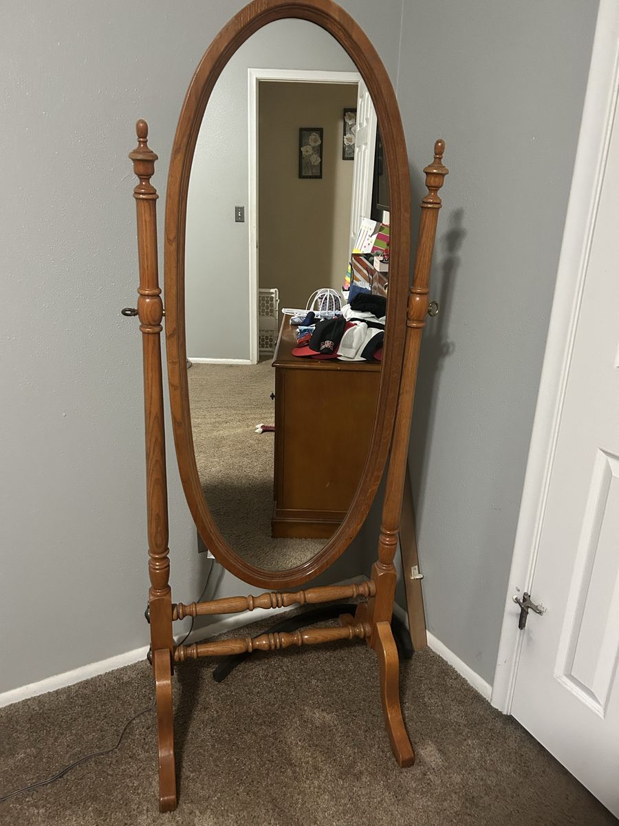 This Crown Mark cheval mirror features an oak finish and a tilting oval design for adjustable viewing angles.