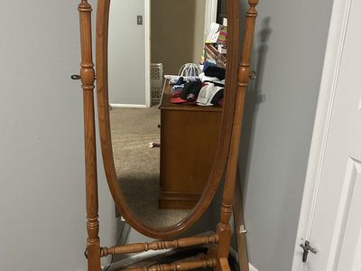 This Crown Mark cheval mirror features an oak finish and a tilting oval design for adjustable viewing angles.