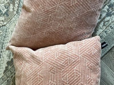 pair of dusty rose pink throw pillows featuring an intricate geometric triangle and diamond woven jacquard pattern.