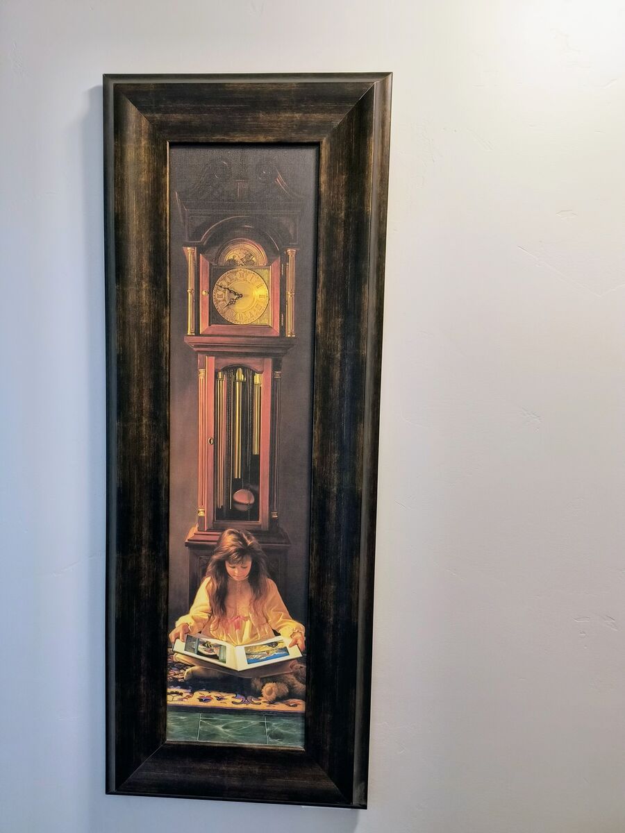 Wood framed picture of girl reading by grandfather clock