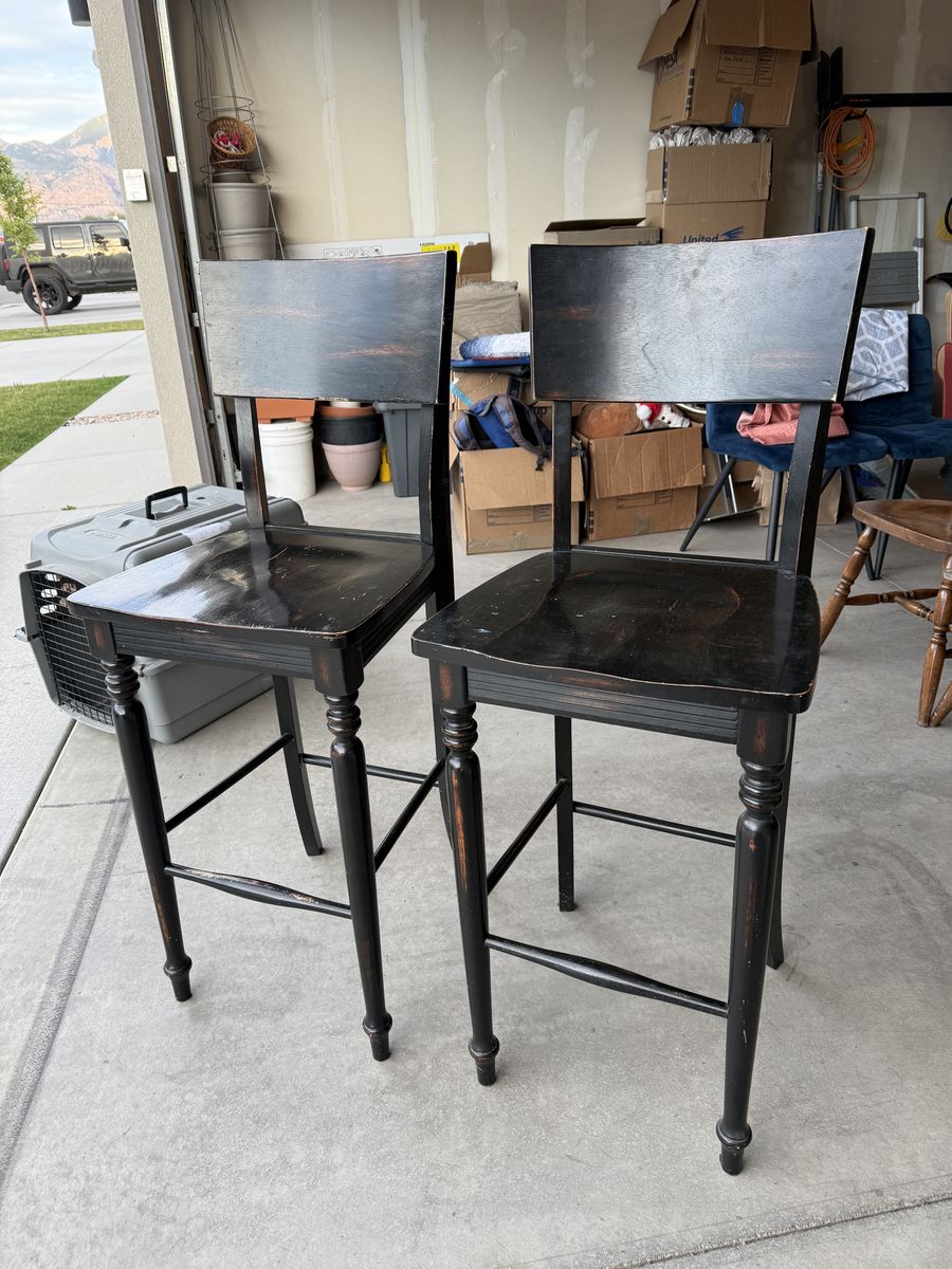 Pair of distressed black farmhouse-style wood bar stools.