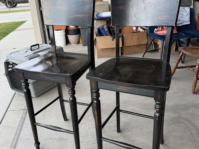 Pair of distressed black farmhouse-style wood bar stools.