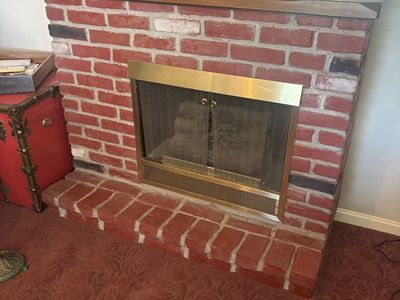 Red Brick Fireplace with Wooden Mantle and Brass Fire Screen.