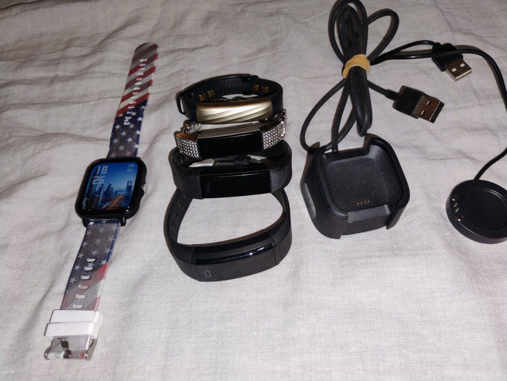 Fitbits and a generic brand Fitbit and a smart watch and a couple smart watch chargers.
