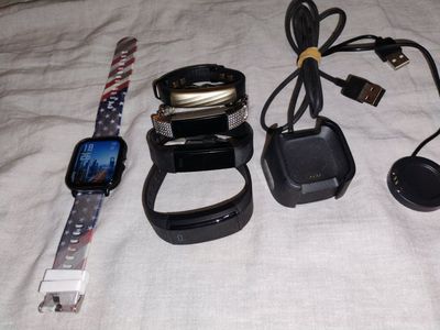 Fitbits and a generic brand Fitbit and a smart watch and a couple smart watch chargers.