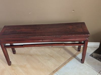 This dark red Chinese wine table features a rectangular top and tapered legs joined by stretchers.