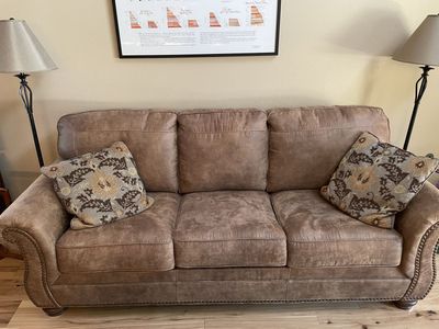 Ashley Furniture couch in a leather-like fabric with curved arms, wooden feet and metal trim